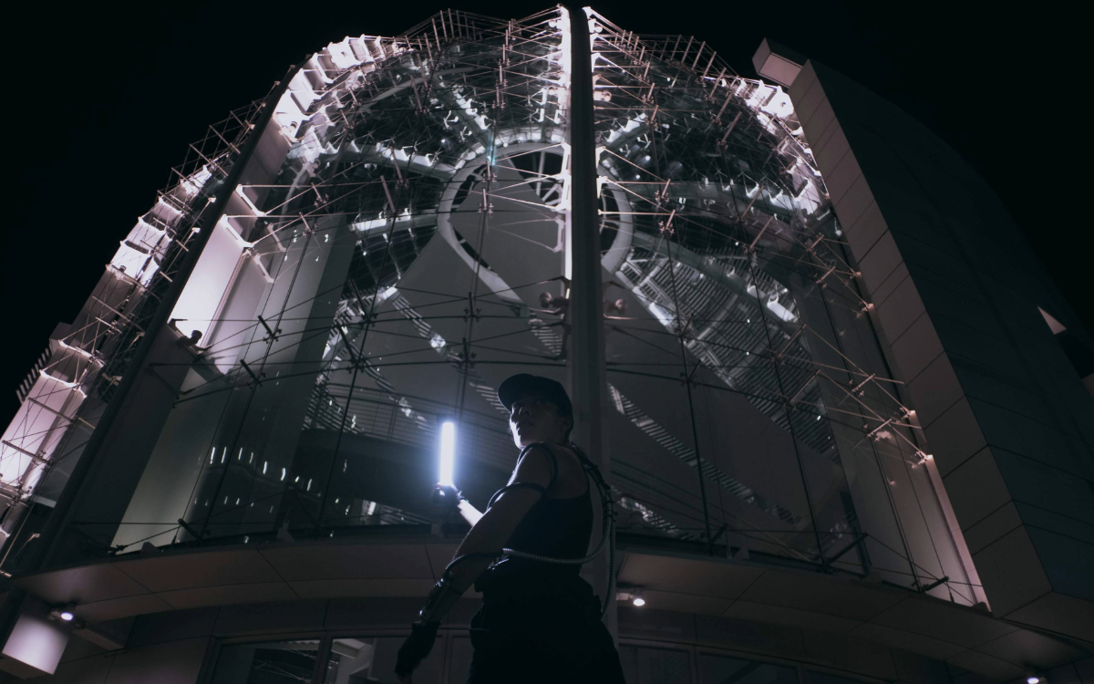 Shannon in technical gear in front of futuristic building at night
